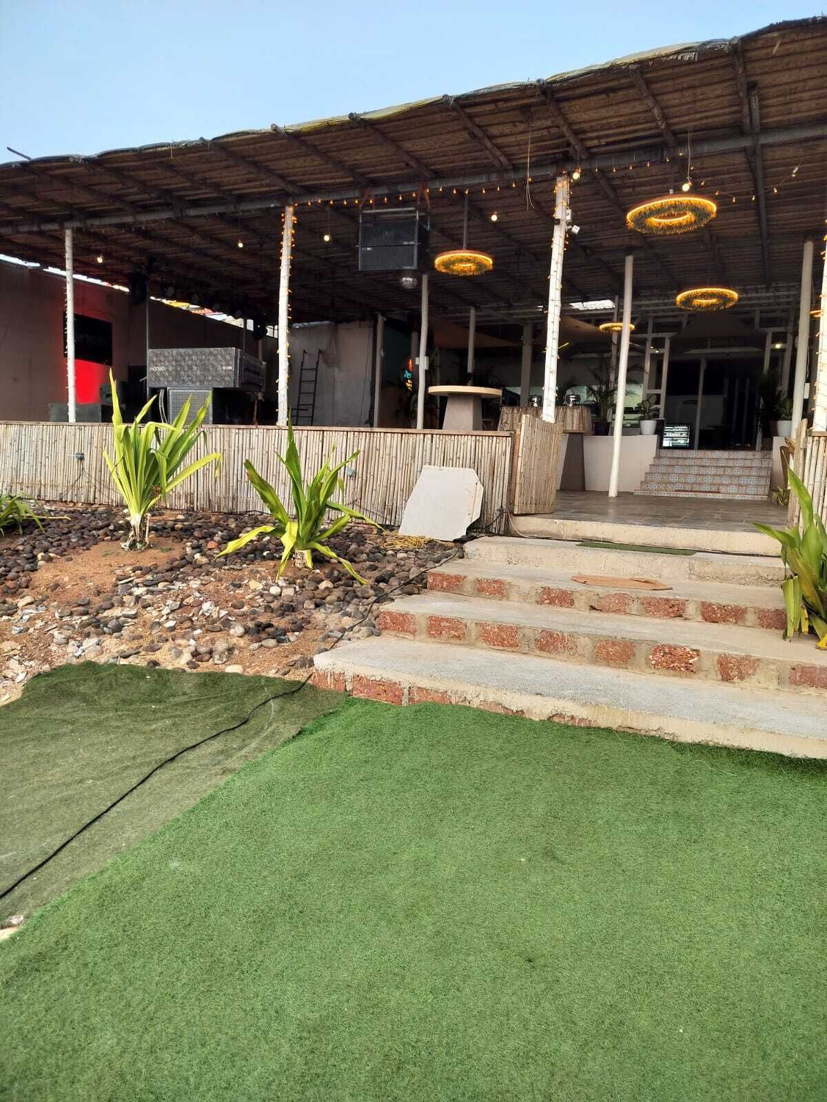 A building with a covered outdoor area, steps leading to a door, and string lights hanging from the ceiling.