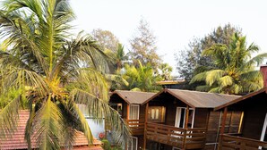 A pool surrounded by palm trees and wooden buildings with balconies. - Surf House Beach Resort (Baga)