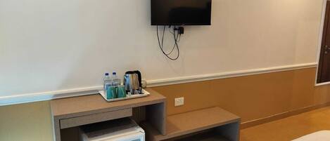 A hotel room with a bed, a small refrigerator, a TV mounted on the wall, and a tray with bottles and cups.