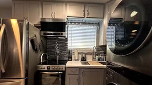 A compact kitchen with stainless steel appliances, a built-in oven, and a window with blinds. - Welcome to SD Cozy Home - B (La Mesa)