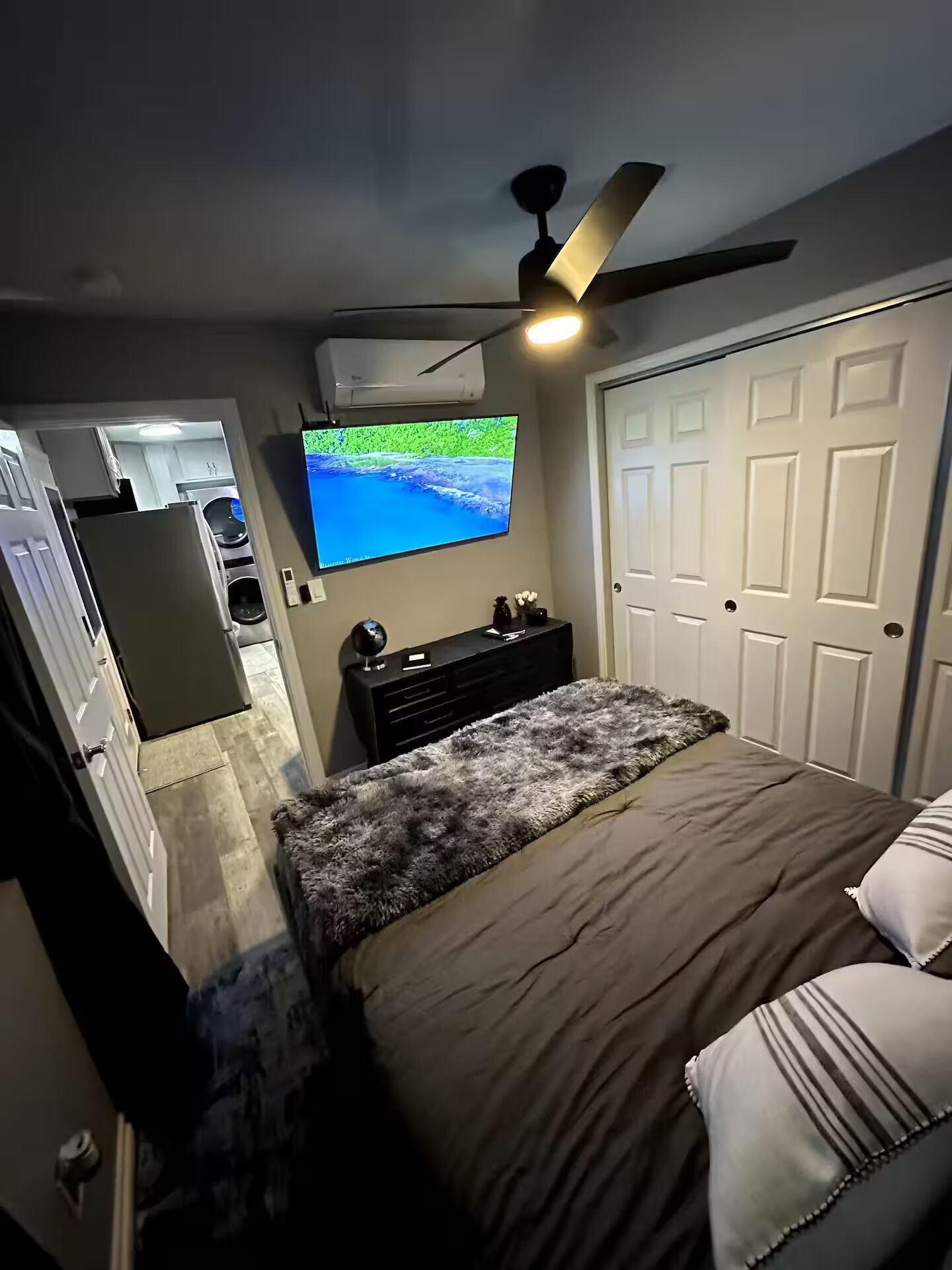 Une chambre à coucher avec un lit, un téléviseur fixé au mur, un ventilateur de plafond et une porte.