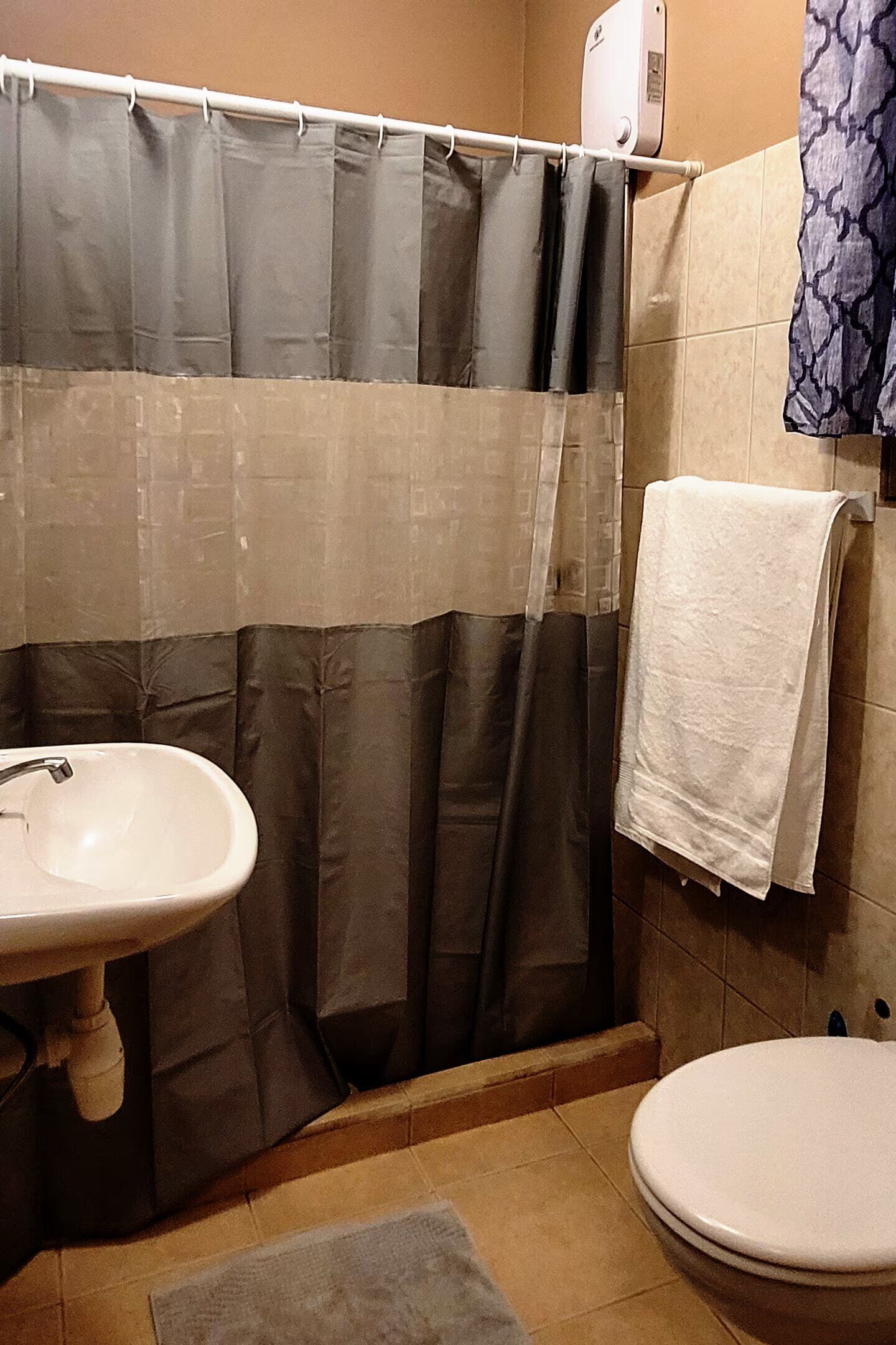 Ein Badezimmer mit Duschvorhang, Waschbecken, Toilette und einem Handtuch, das an der Wand hängt.