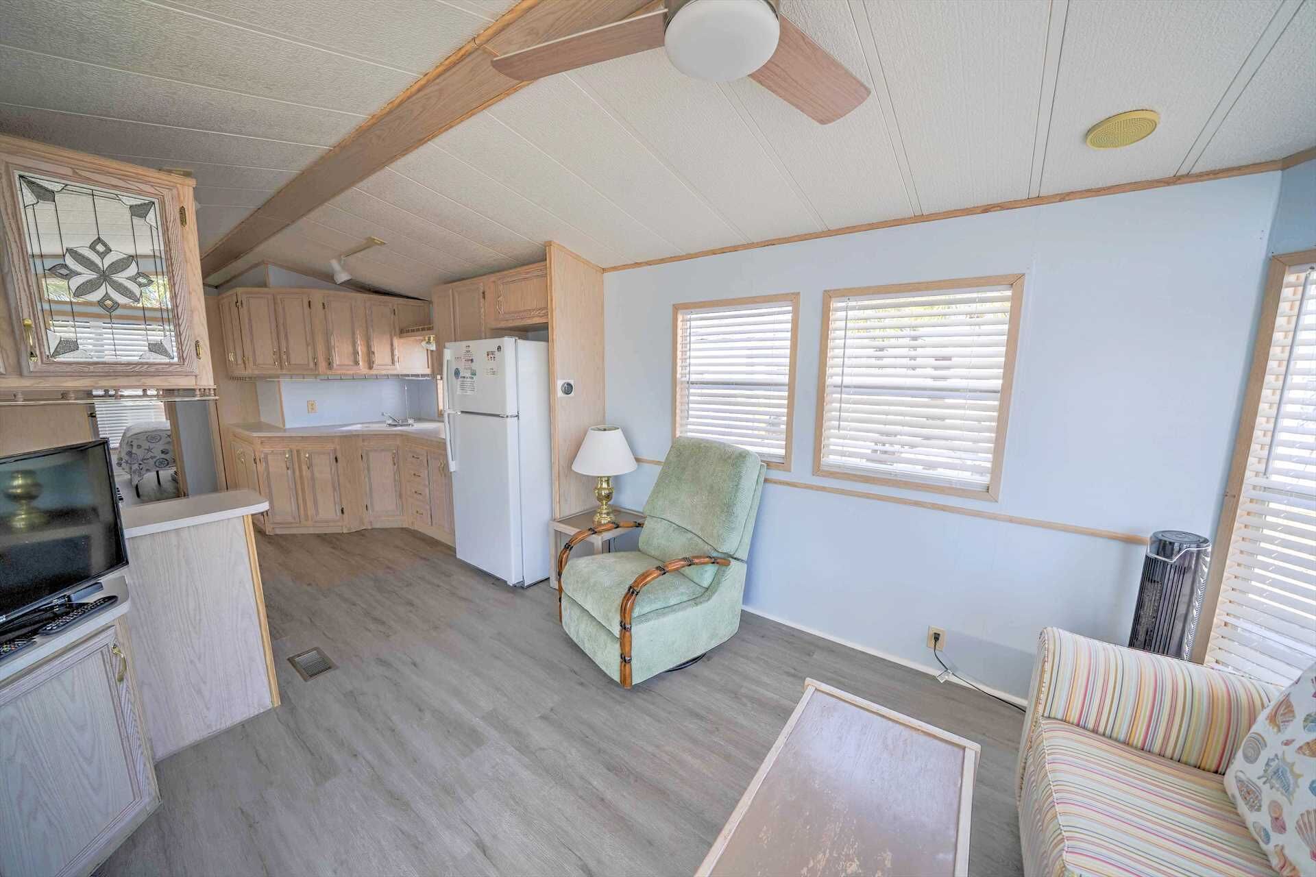 A compact living space with a kitchenette, a green armchair, a striped sofa, and a ceiling fan.