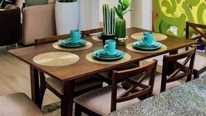 A dining area with a wooden table set for four, surrounded by chairs. There is a large potted plant and a cactus on the table.