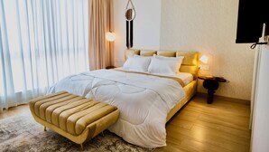A modern bedroom with a large bed, bedside lamps, a round mirror, and a wooden floor.