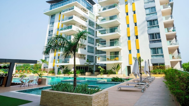 A modern hotel with multiple balconies, a swimming pool, and outdoor seating areas.