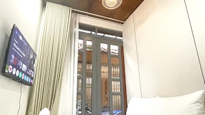 A hotel room with a bed, a TV mounted on the wall, a window with curtains, and a door with a metal gate. - Luxhome (Ho Chi Minh City)