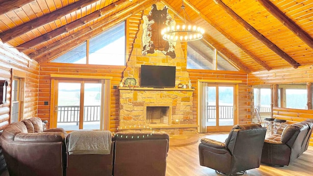 A log cabin interior with a stone fireplace, leather sofas, and a large chandelier.