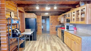 A log cabin interior with a kitchen area featuring wooden cabinets, a refrigerator, and a microwave.