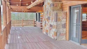A wooden deck with a stone wall and glass doors.