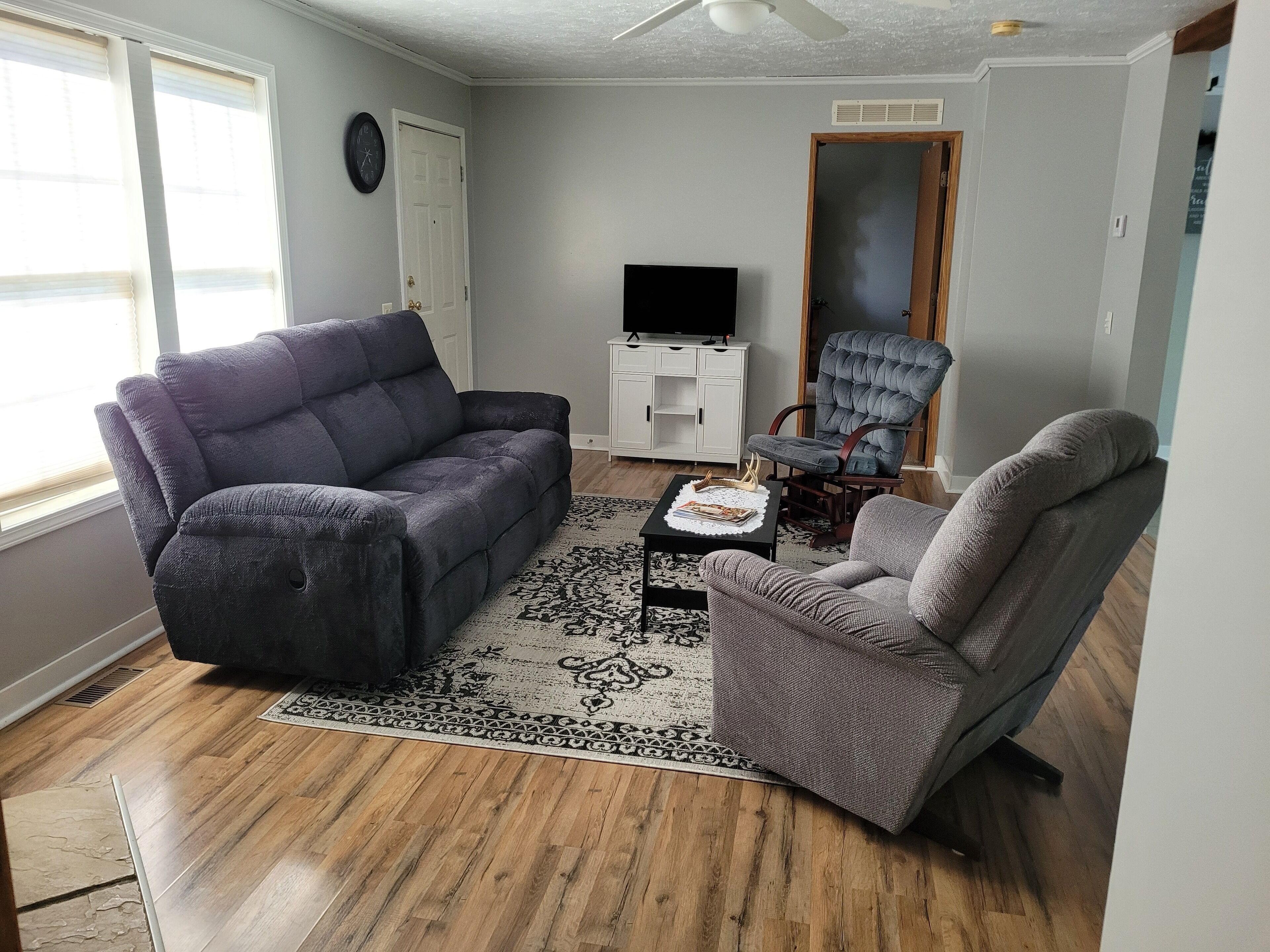 A living room with a gray sofa, a gray armchair, a small table with a decorative item, and a flat-screen TV on a white cabinet.
