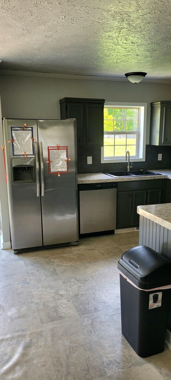 A kitchen with stainless steel appliances, a window, and a trash bin.