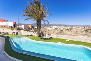Uma piscina com uma palmeira, um espaço de pátio e vista para uma cidade ao fundo.