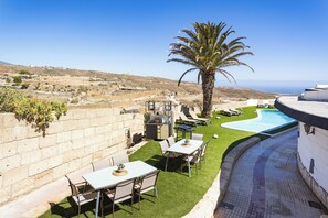 Área de piscina no terraço com palmeira, mobiliário ao ar livre e vista para a paisagem.