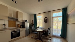 Eine moderne Küche mit Essbereich, Holzboden und großen Fenstern mit Vorhängen.