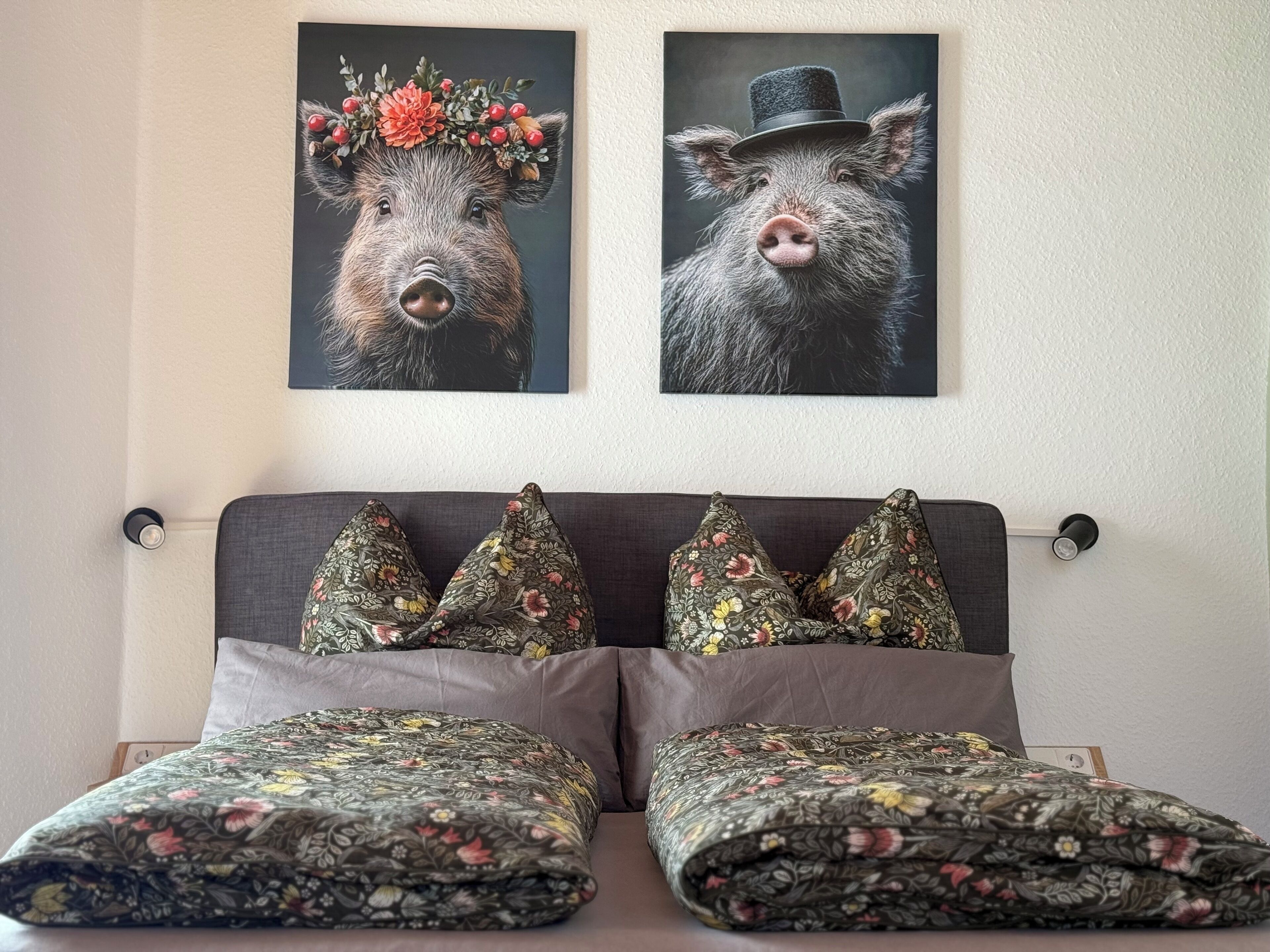 A bed with floral-patterned bedding and pillows, a dark headboard, and two wall-mounted pictures of pigs.