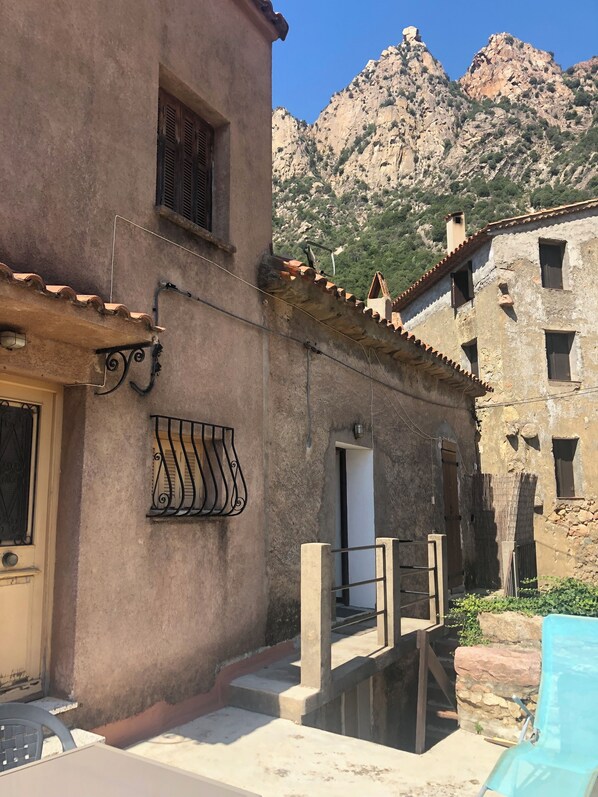 A rustic building with a stone facade, a metal balcony, and a view of rocky mountains. - Haven of peace (Ota)