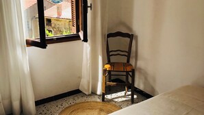 A room with a bed, a chair, a window with curtains, and a view of a mountainous landscape.