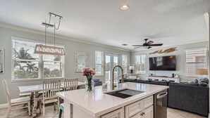 A spacious kitchen with a large island, a dining area with a table and chairs, a living room with a sofa and TV, and large windows with blinds. - Location! Family Friendly, Pool, Elevator, Close to Beach (Holmes Beach)