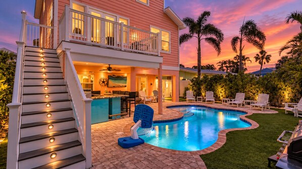 A two-story house with a swimming pool, outdoor seating, and a staircase with lights.
