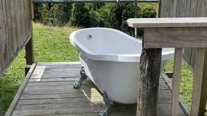 Una terraza de madera con una bañera blanca, barandillas de madera y vistas a un paisaje verde.