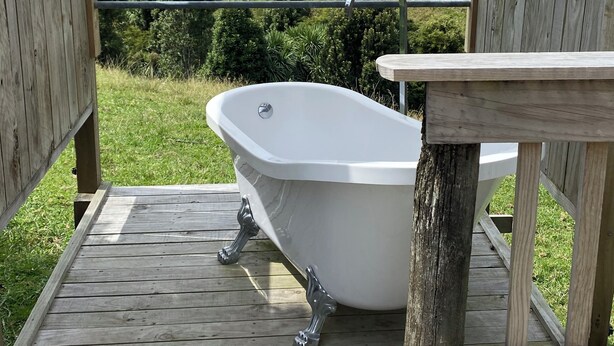 Een houten terras met een wit bad, houten leuningen en uitzicht op een groen landschap.