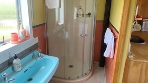 Een badkamer met douche, wastafel en raam.