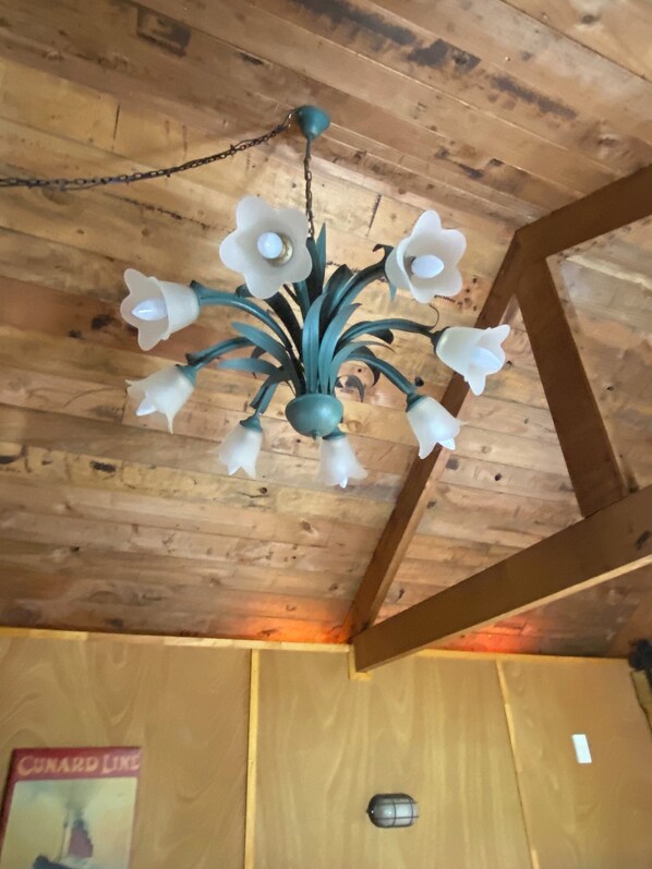 Eine Holzbalkendecke mit einem Kronleuchter, der mehrere weiße Blumen und ein turquoisefarbenes Mittelstück zeigt.