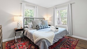 A bedroom with a bed, nightstands, a lamp, a window, and a patterned rug.