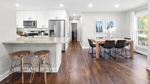 A modern kitchen with white cabinets, stainless steel appliances, and a wooden dining area with a table and chairs.