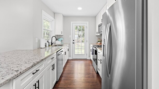 A modern kitchen with white cabinetry, a stainless steel refrigerator, and a wooden floor.
