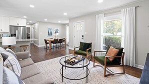 A modern living room with a sofa, a coffee table, and a dining area in the background.