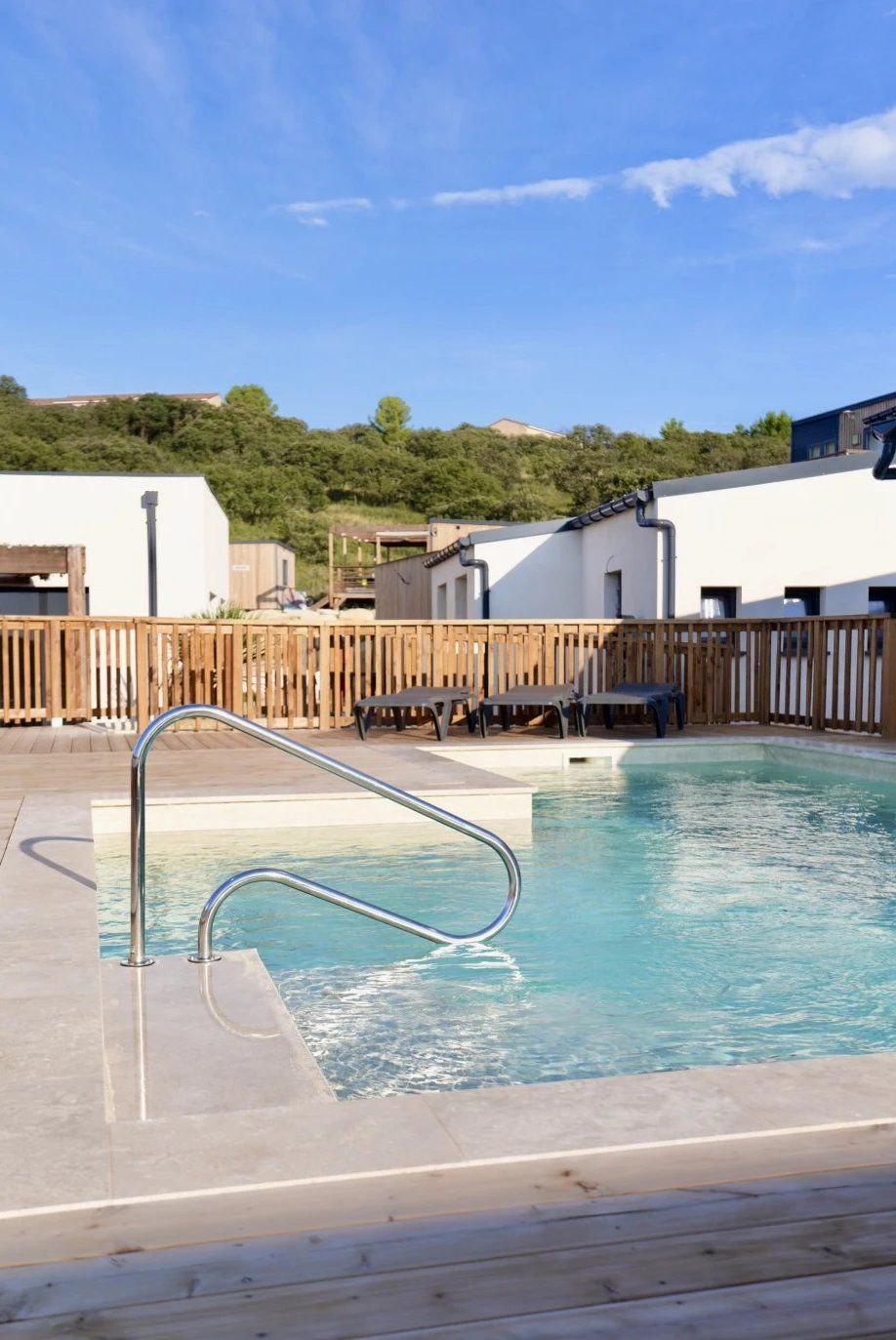 A swimming pool with a wooden deck, a metal ladder, and a wooden fence.