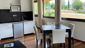 A modern kitchen with white cabinets, a microwave, and a dining area with a dark wooden table and white chairs. - ZEcamping 3* locatif TV clim 41m2 4 pers (Saint-Lizier)
