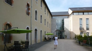 A courtyard with outdoor seating and a building entrance. - ZEcamping 3* locatif TV clim 41m2 4 pers (Saint-Lizier)