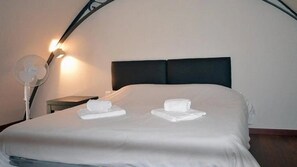 A hotel room with a bed, a nightstand, a lamp, and a fan.