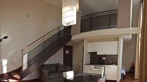 A modern interior with a staircase leading to a loft area, a dining table, and a kitchen with white cabinets.