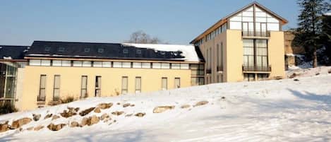 A modern building with a flat roof and large windows, surrounded by snow.