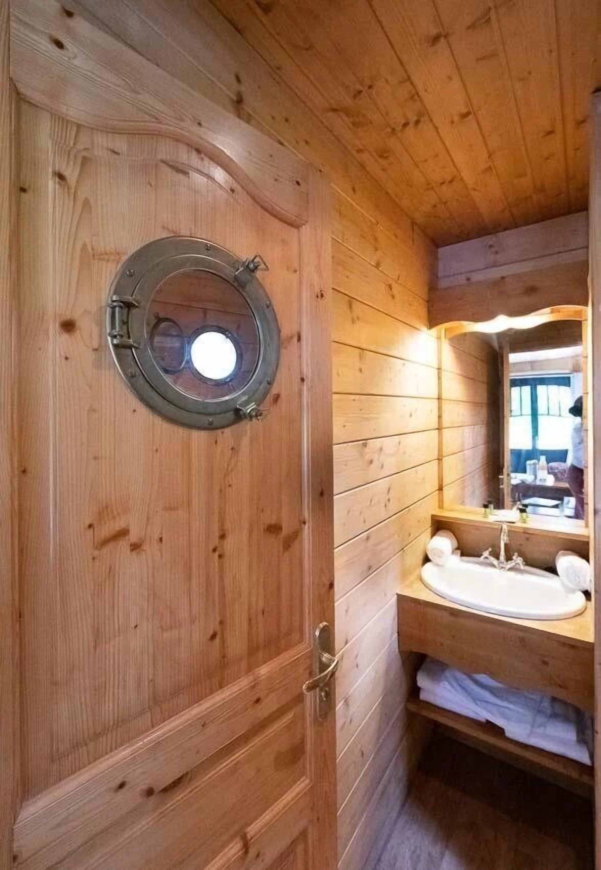 Un bagno in una cabina di legno con una finestra rotonda, un lavandino e uno specchio.