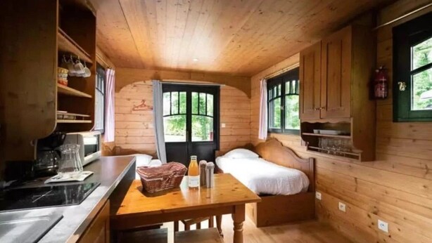 Interior acolhedor de uma cabana com decoração em madeira, uma cama, uma mesa de jantar e uma área de cozinha.