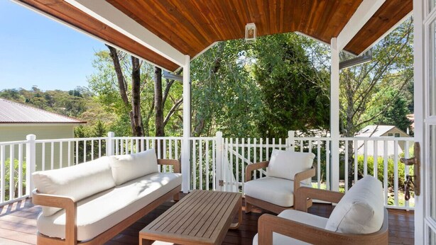 A covered outdoor seating area with wooden furniture and a white fence.