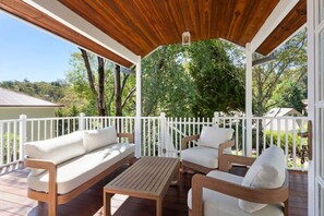 A covered outdoor seating area with wooden furniture and a white fence.