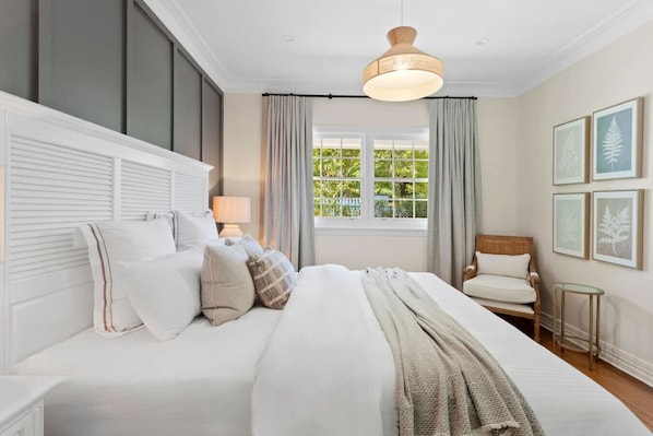A bedroom with a large bed, a bedside table with a lamp, a chair, and a window with curtains.