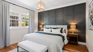 A bedroom with a large bed, bedside lamps, a bench, and a view through a window.