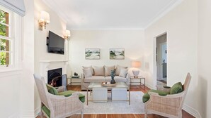 A living room with a fireplace, a sofa, two armchairs, a coffee table, and wall-mounted artwork.