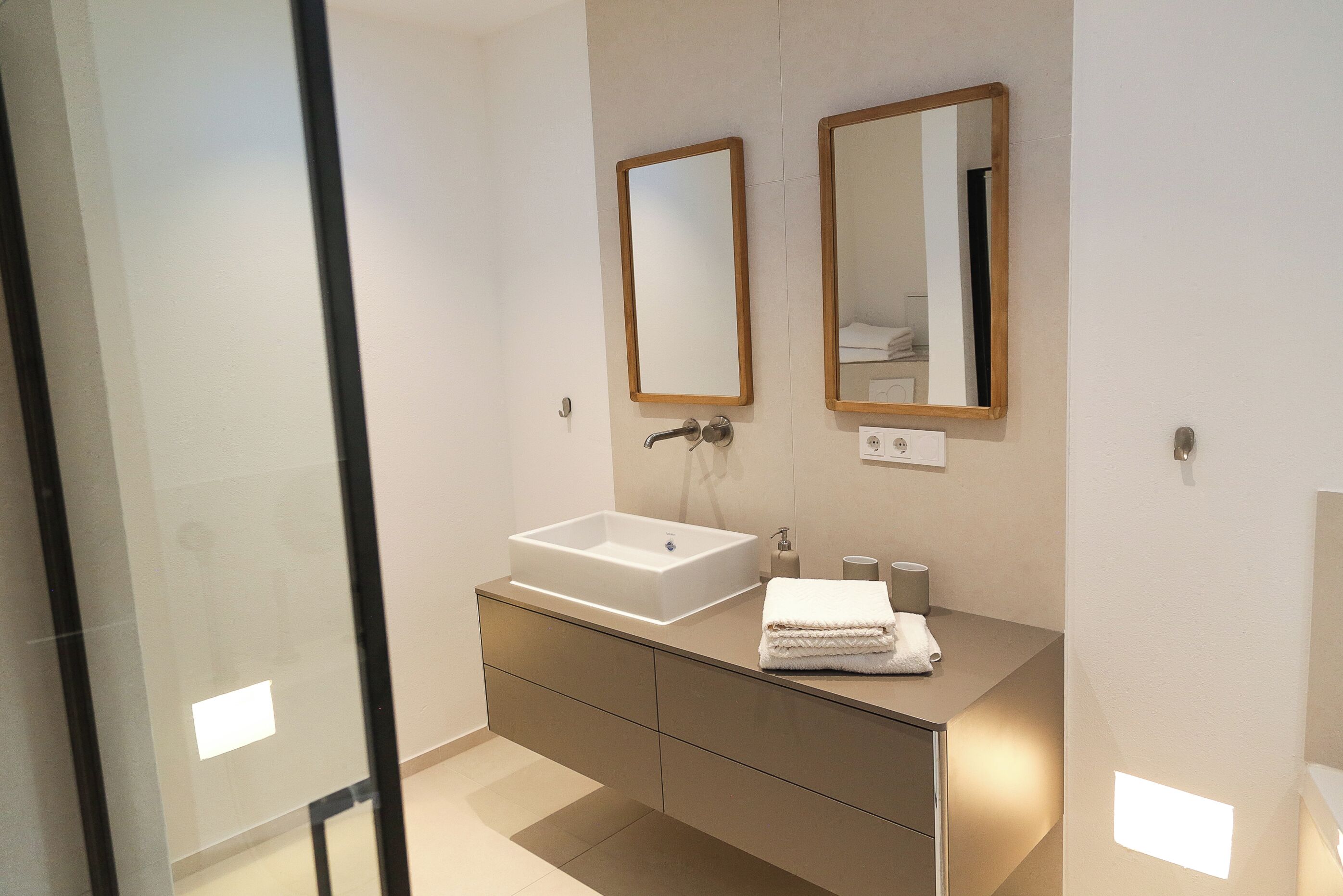 Une salle de bain moderne avec un grand lavabo, deux miroirs et un meuble-lavabo doté de tiroirs.
