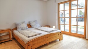 A wooden bed with a headboard, two bedside tables, and a large window with a view of the outside. - Exclusive vacation apartment in Chiemgau (Obing)