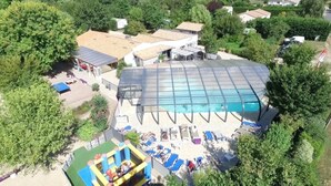 Ett flygbildsbild av ett semesterområde med en stor swimmingpool, solstolar och en liten lekplats för barn.