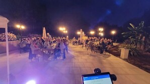 An outdoor dining area with multiple tables and chairs, surrounded by plants and illuminated by overhead lights. - ZEcamping 3 étoiles pataugeoire mobil-home 24m2 (Pezuls)