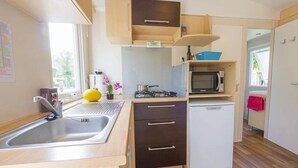 A compact kitchen with a sink, stove, microwave, and a small refrigerator. - ZEcamping 3 étoiles pataugeoire mobil-home 24m2 (Pezuls)